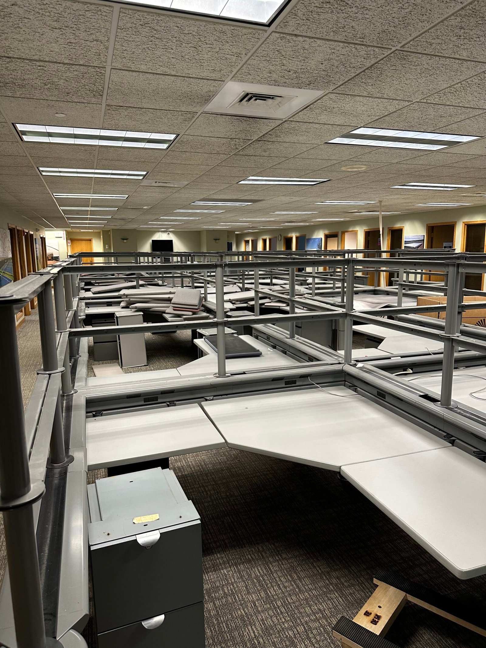 Office cubicles being deconstructed with panels removed, showing a partially dismantled workspace.