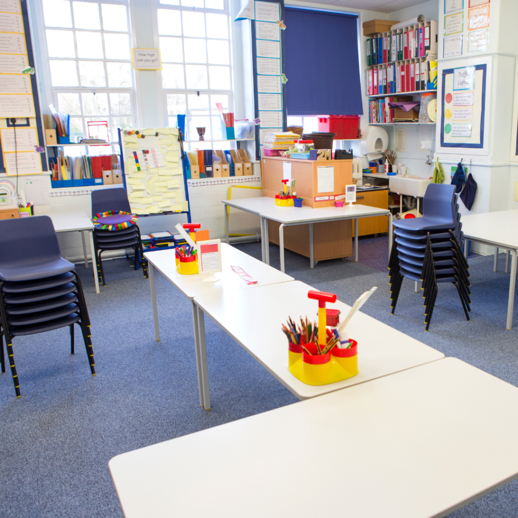 Classroom with learning tables, stacked chairs, and various educational materials and furniture.