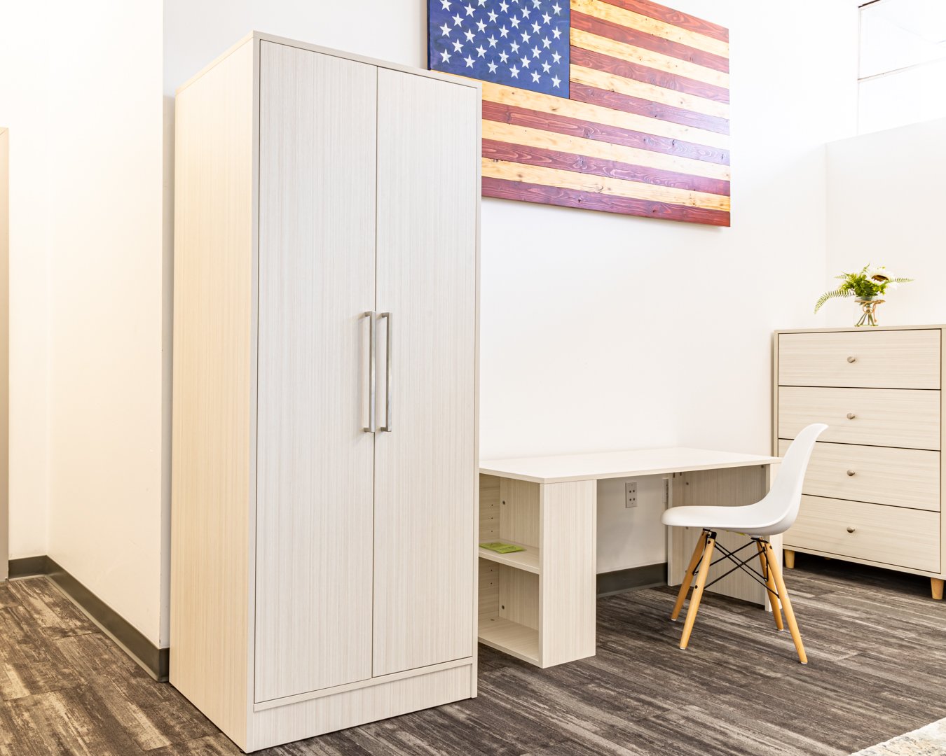 American-made light-colored armoire, desk, and dresser with CNC machine craftsmanship, featuring the American flag in the background