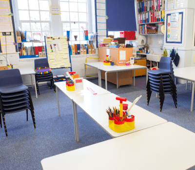 Classroom with learning tables, stacked chairs, and various educational materials and furniture.